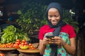 Young african woman selling in a local market smiling while using her mobile phone