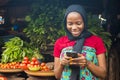 Young african woman selling in a local market smiling while using her mobile phone