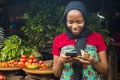 Young african woman selling in a local market smiling while using her mobile phone