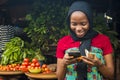 Young african woman selling in a local market smiling while using her mobile phone Royalty Free Stock Photo