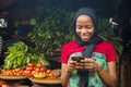 Young african woman selling in a local market smiling while using her mobile phone