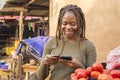 young african woman selling in a local african market using her mobile phone and credit card to do a transaction online smiling