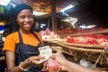Young black woman selling tomatoes in a local african market collecting money from a paying customer