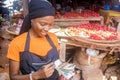Pretty african woman selling tomatoes in a local african market smiling while counting money. Royalty Free Stock Photo