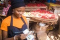 Pretty young african woman selling tomatoes in a local african market counting money and smiling Royalty Free Stock Photo