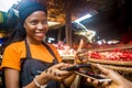 Pretty young black woman selling tomatoes in a local african market receiving payment via mobile phone transfer giving a thumbs up Royalty Free Stock Photo