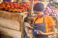 Young african woman selling tomatoes in a local african market using her mobile phone and holding a mobile pos device.