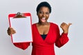 Young african woman with short hair holding clipboard with blank space pointing thumb up to the side smiling happy with open mouth Royalty Free Stock Photo