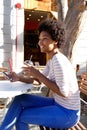 Young african woman sitting outside cafe with cell phone Royalty Free Stock Photo