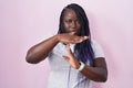 Young african woman standing over pink background doing time out gesture with hands, frustrated and serious face Royalty Free Stock Photo