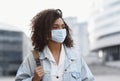 Young african woman wearing protective face mask in a city. Mixed race student girl on a city street.