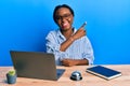 Young african woman working at hotel reception using laptop with a big smile on face, pointing with hand and finger to the side Royalty Free Stock Photo