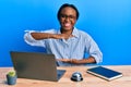 Young african woman working at hotel reception using laptop gesturing with hands showing big and large size sign, measure symbol Royalty Free Stock Photo