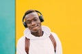 Young afro American black man listening music with wireless headphones while wearing a white sweatshirt and a backpack Royalty Free Stock Photo