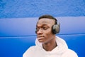 Young afro American black man listening music with wireless headphones while wearing a white sweatshirt, looking to the side Royalty Free Stock Photo