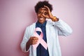 Young afro american doctor man holding cancer ribbon standing over isolated pink background with happy face smiling doing ok sign Royalty Free Stock Photo