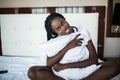 Young beautiful afro american girl smiling while lying in bed hugging pillow at home Royalty Free Stock Photo