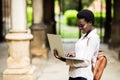 Young afro american girl student with laptop typing outdoors in campus.