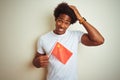 Young afro american man holding China Chinese flag standing over isolated white background stressed with hand on head, shocked Royalty Free Stock Photo