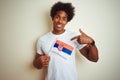 Young afro american man holding Serbia Serbian flag standing over isolated white background with surprise face pointing finger to Royalty Free Stock Photo