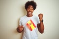 Young afro american man holding Spain Spanish flag standing over isolated white background screaming proud and celebrating victory