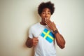 Young afro american man holding Sweden Swedish flag standing over isolated white background cover mouth with hand shocked with Royalty Free Stock Photo