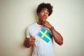 Young afro american man holding Sweden Swedish flag standing over isolated white background serious face thinking about question, Royalty Free Stock Photo