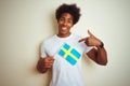 Young afro american man holding Sweden Swedish flag standing over isolated white background with surprise face pointing finger to Royalty Free Stock Photo