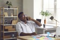 Young Afro American businessman sitting at office desk and talking on mobile phone Royalty Free Stock Photo