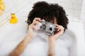 Young afro-american teen girl laying in bath with foam, wearing swag jewelry flawless, making selfie Royalty Free Stock Photo