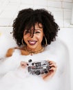 Young afro-american teen girl laying in bath with foam, wearing swag jewelry flawless, making selfie Royalty Free Stock Photo