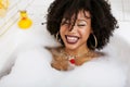 Young afro-american teen girl laying in bath with foam, wearing swag jewelry flawless, making selfie Royalty Free Stock Photo