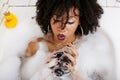 Young afro-american teen girl laying in bath with foam, wearing swag jewelry flawless, making selfie Royalty Free Stock Photo