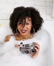 Young afro-american teen girl laying in bath with foam, wearing swag jewelry flawless, making selfie Royalty Free Stock Photo