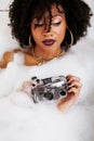 Young afro-american teen girl laying in bath with foam, wearing swag jewelry flawless, making selfie Royalty Free Stock Photo