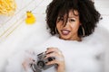 Young afro-american teen girl laying in bath with foam, wearing swag jewelry flawless, making selfie Royalty Free Stock Photo