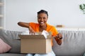 Young Afro woman opening cardboard box, satisfied with good delivery service, receiving online store order at home Royalty Free Stock Photo