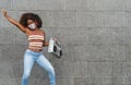 Young Afro woman wearing face mask dancing outdoor while listening to music with wireless headphones and vintage boombox Royalty Free Stock Photo