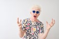 Young albino blond man wearing colorful t-shirt and sunglasses over isolated red background crazy and mad shouting and yelling Royalty Free Stock Photo