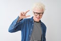 Young albino blond man wearing denim shirt and glasses over isolated white background smiling and confident gesturing with hand Royalty Free Stock Photo