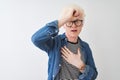 Young albino blond man wearing denim shirt and glasses over isolated white background Touching forehead for illness and fever, flu