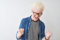 Young albino blond man wearing denim shirt and glasses over isolated white background very happy and excited doing winner gesture Royalty Free Stock Photo