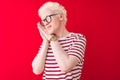 Young albino blond man wearing striped t-shirt and glasses over isolated red background sleeping tired dreaming and posing with