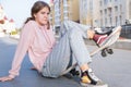 Young alternative teenager girl skater sitting on board on the city street looking away. Royalty Free Stock Photo