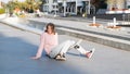 Young alternative teenager girl skater sitting on board on the city street looking away. Royalty Free Stock Photo