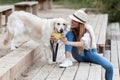 Young amateur photograph woman taking a photo of her dog sitting near the river in the park