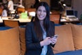 Young American business woman sitting at her sofa, using phone in her office and smiling Royalty Free Stock Photo