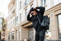 Young American hipster man in trendy cap in a black sweatshirt in stylish sunglasses in jeans with a leather backpack Royalty Free Stock Photo