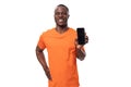 young american man in orange t-shirt holding smartphone screen forward with mockup Royalty Free Stock Photo