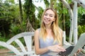 Young american woman resting on swing and using laptop, palms in background. Royalty Free Stock Photo